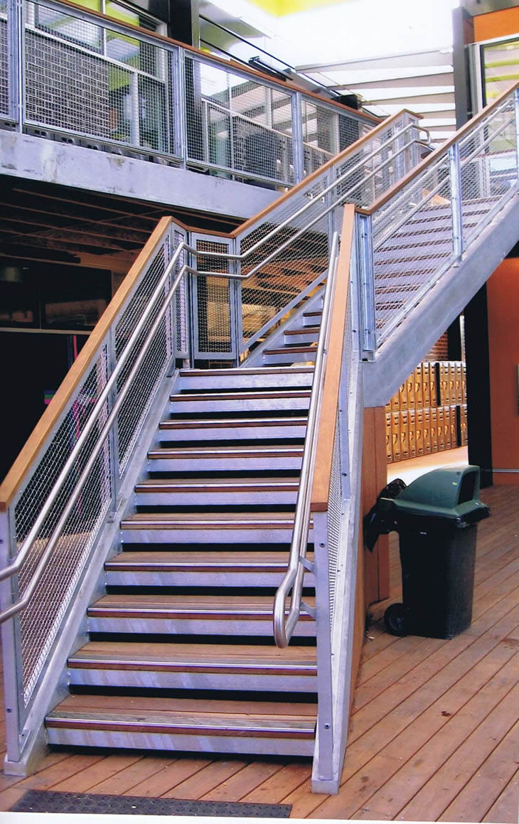 Steel stair case with mesh side panels and wood top rail